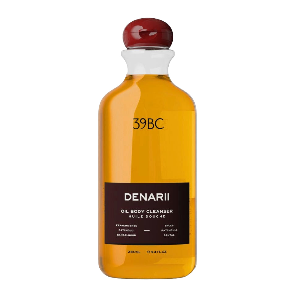 A 280ml glass bottle of DENARII 39BC Oil Body Cleanser, filled with amber-colored liquid and featuring a black label with a dark red stopper, set against a plain white background.