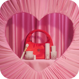 Red handbag with cosmetic products on a pink heart-shaped background
