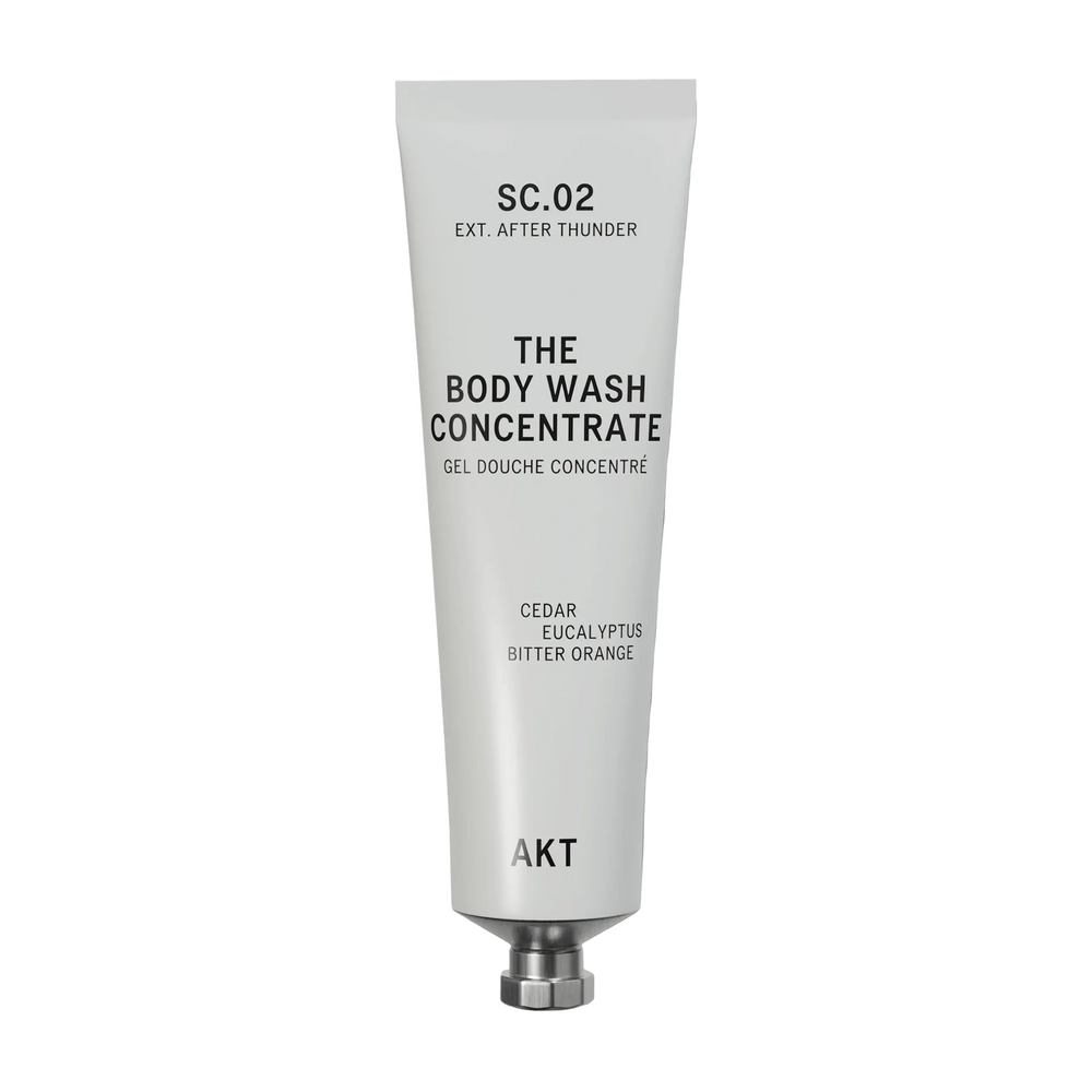 A white squeeze tube of AKT London body wash concentrate, SC.02, with black text, shown on a light gray background with a soft shadow.