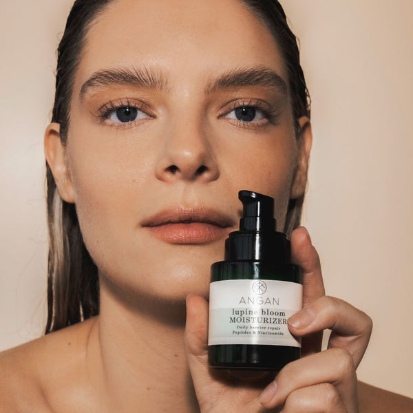 Woman holding a bottle of ANGAN lupine bloom moisturizer against a neutral background