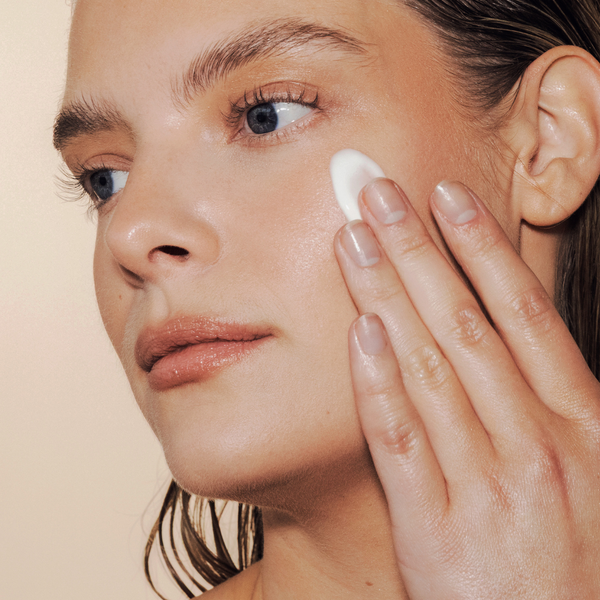 Woman applying cream to her face with a neutral background