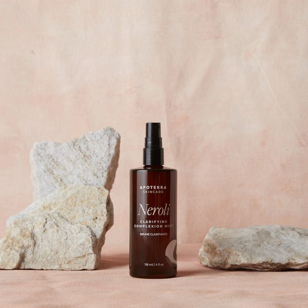 A bottle of Apoterra Skincare Neroli product on a pink background with rocks.