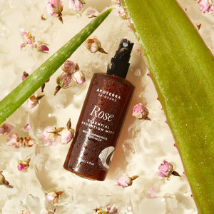 Rose essential hydration mist bottle on a textured surface with flowers and aloe vera leaves.