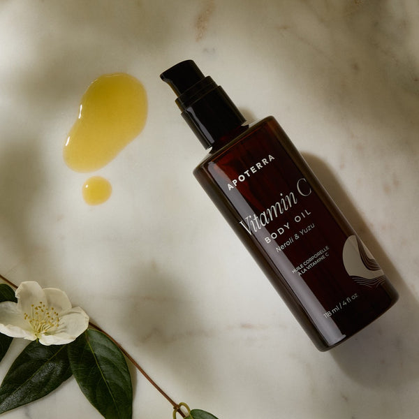 Aoterra Vitamin C body oil bottle on a marble surface with a flower and oil droplets.