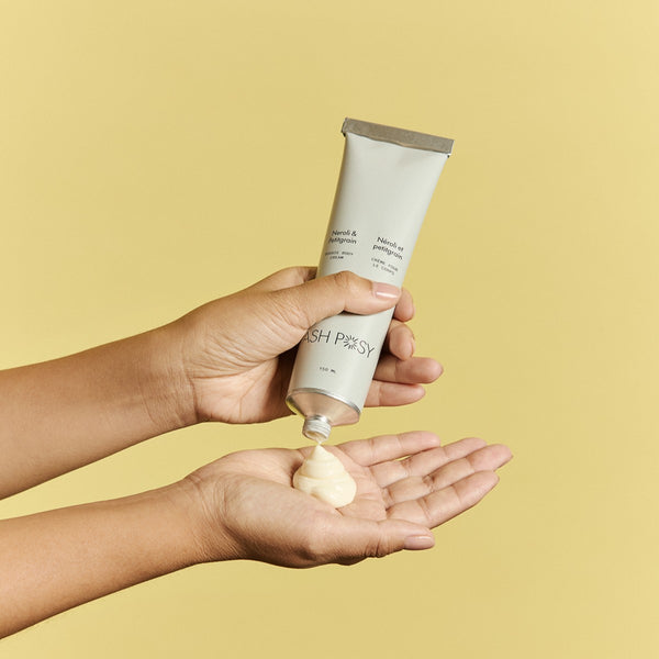 Hand holding a tube of lush body cream from Ash Posy against a yellow background