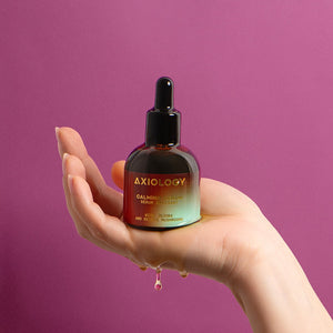 Hand holding Axiology serum bottle with dropper against a purple background