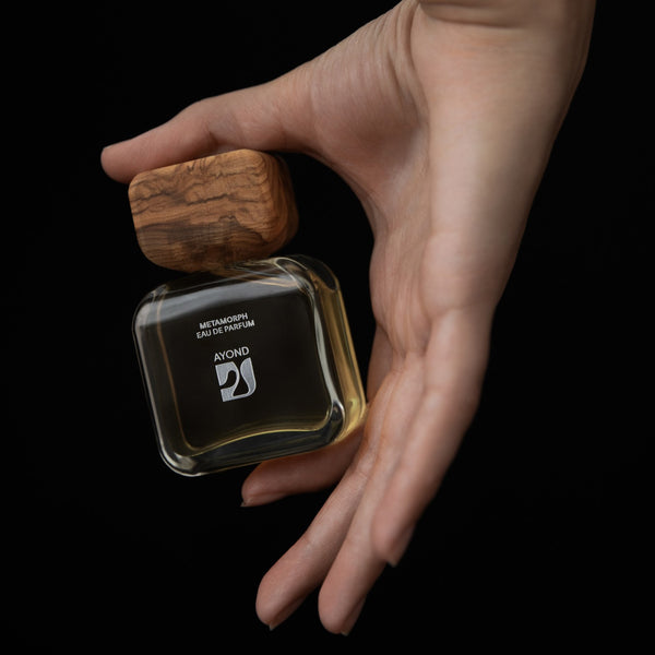 Hand holding Ayond perfume bottle with wooden cap against a black background