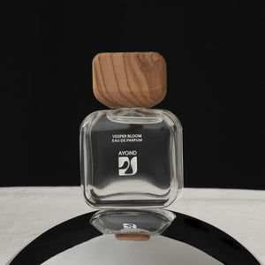 Clear perfume bottle with wooden cap from Ayond on a reflective surface