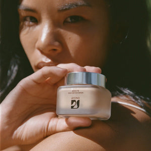 woman holding a jar of Ayond Zeolite AHA Detox Mask with a blurred background