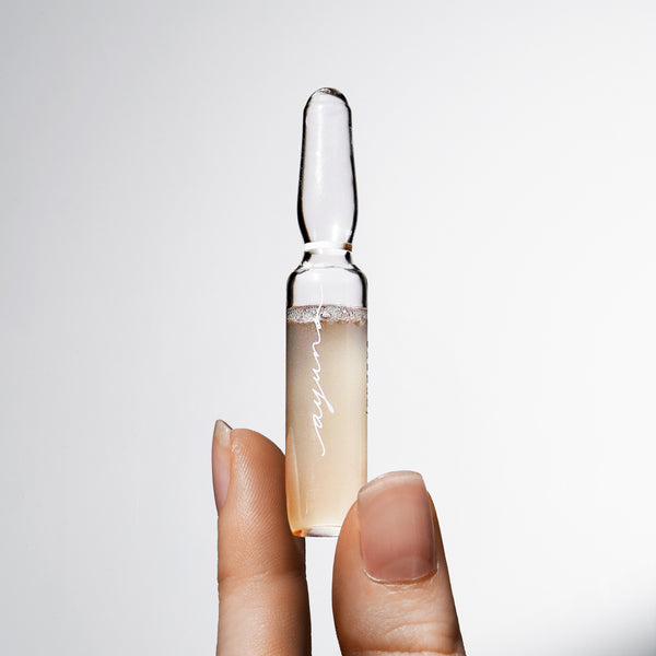 Hand holding a skincare ampoule with a clear liquid against a white background