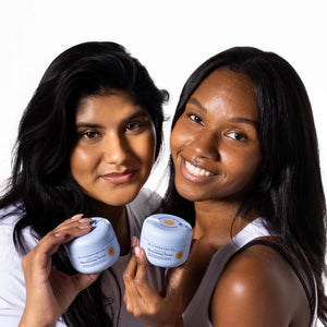 Two women holding and showing a skincare product against a white background