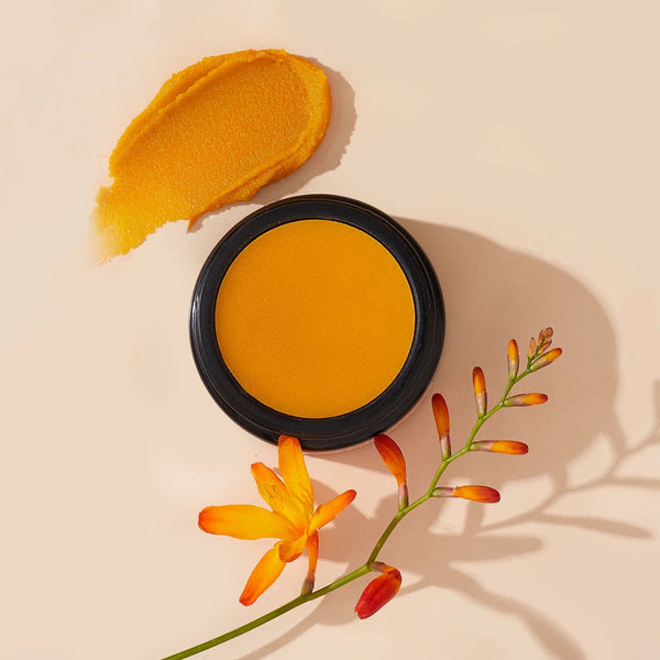 Yellow face balm Solace from By Achilles in a round black glass jar with a floral branch on a beige background