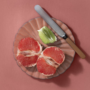 Sliced grapefruit and lime on a decorative plate with a knife against a pink background