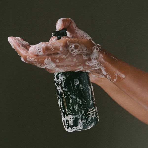 Hand holding a black bottle with soapy hands against a dark background. CORPUS Aromatic Hand Wash Amalgam 7
