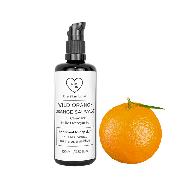 Dry Skin Love Wild Orange Oil Cleanser bottle with orange, vanilla and botanical elements. Next to the black glass bottle with a black pump is an orange. with white background
