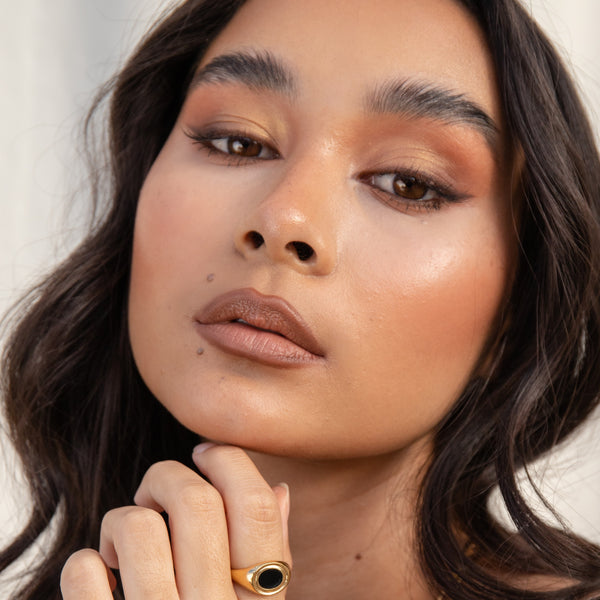 Close-up of a woman with makeup and a gold ring on her finger against a neutral background. EYE OF HORUS Eyeshadow Compact Dawn