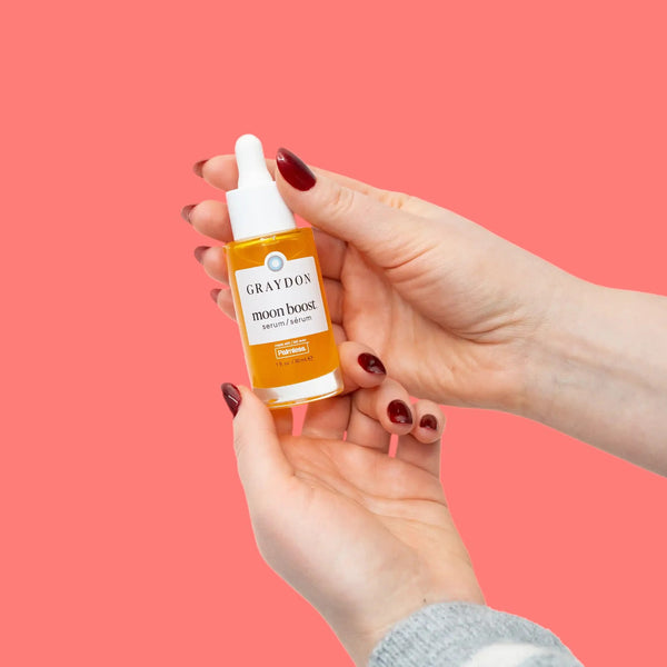 Hand holding a bottle of Graydon moon boost serum against a pink background