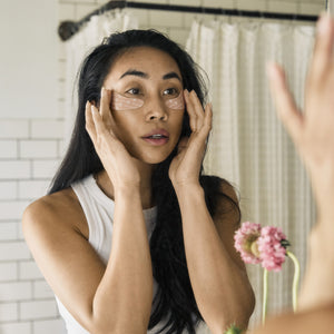 Woman applying eye mask in front of a mirror