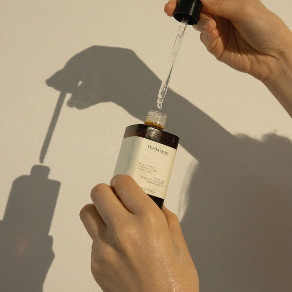 Hand holding a dropper over a bottle of face serum from Hyeja against a neutral background