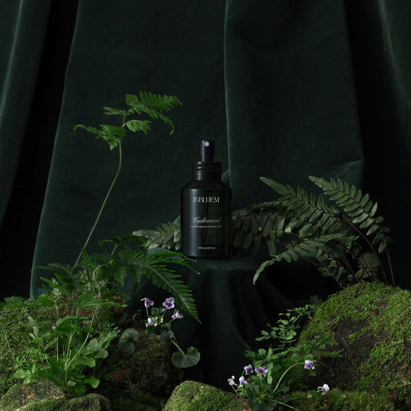 Dark green bottle with dropper labeled 'INBLUEM' surrounded by green plants and moss on a dark background. INBLUEM Hydrosoul Cleansing & Toning Mist