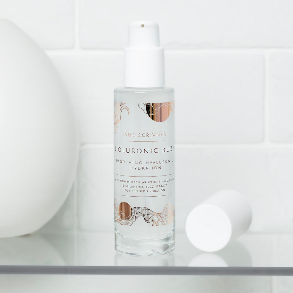 A white pump bottle of Jane Scrivner Bioluronic Blioz Smoothing Hyaluronic Serum, featuring elegant beige and brown abstract floral illustrations on the label, set against a clean white background with a soft shadow.