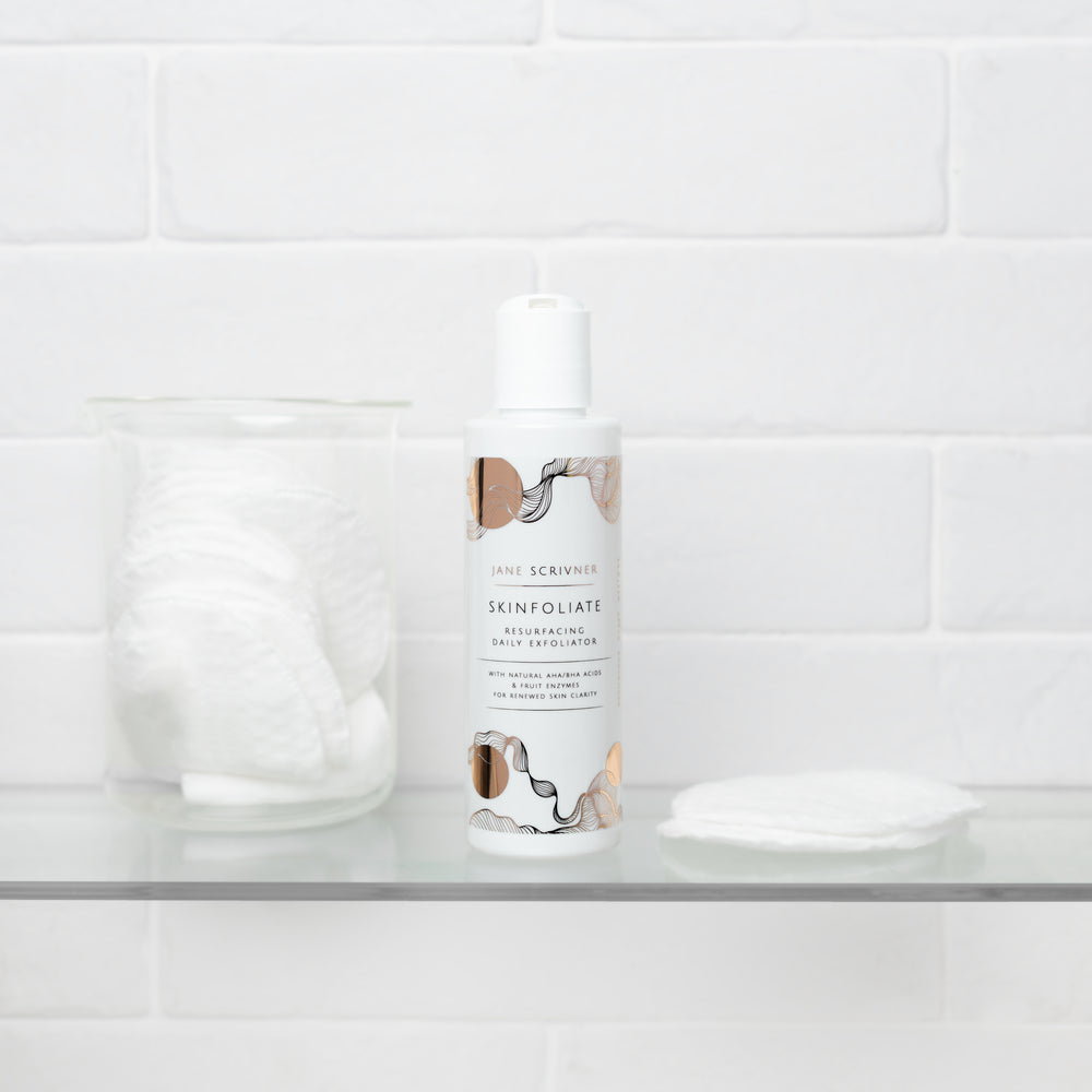A white bottle of Jane Scrivner Skinfoliate Resurfacing Daily Exfoliator with peach and gray botanical illustrations on the label, set against a plain white background with a soft shadow.
