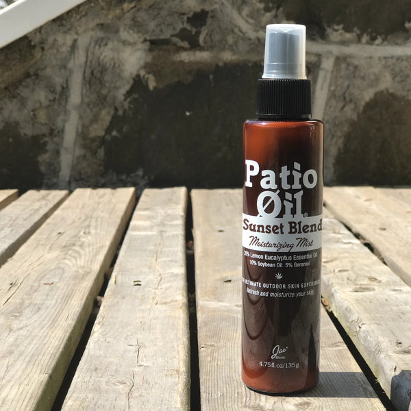 Bottle of 'Patio Oil Sunset Blend' on a wooden surface with a stone wall background