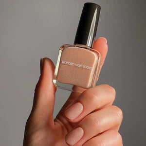 Hand holding a bottle of KAROLIN VAN LOON 45 Crushed Crystals nail polish with a neutral color.