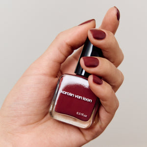 Hand holding a bottle of Karolin van Loon nail polish with a maroon color.