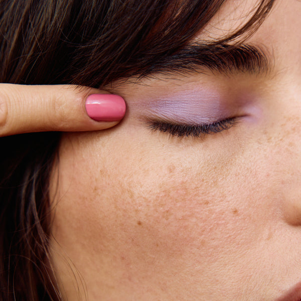 Close-up of a person applying makeup to their eyelid with a pink nail.