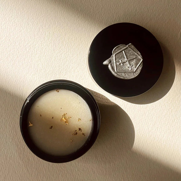 LEPAAR Night Milk Contour Balm Rejuvenating Face Refine in black glass jar. It is open and you can see the off white balm with golden particles. On light beige textured background