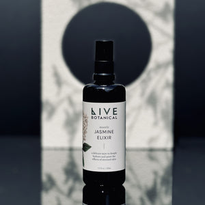 Bottle of Live Botanical Jasmine Elixir on a reflective surface with a geometric background