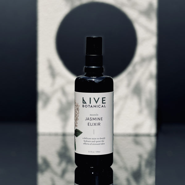 Bottle of Live Botanical Jasmine Elixir on a reflective surface with a geometric background