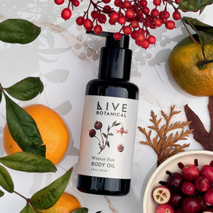 LIVE Botanical winter sun body oil bottle surrounded by fruits and leaves on a light background