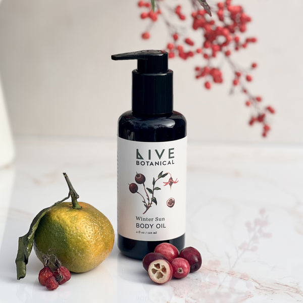 Bottle of Live Botanical Winter Sun Body Oil with an orange and berries on a light background