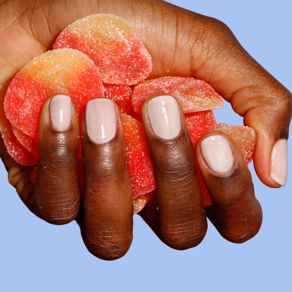 Hand holding gummy candies against a blue background and showing her nails in sheer creamy white color