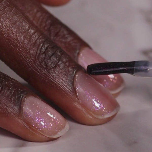 Close-up of a hand with pink glittery nail polish being applied.