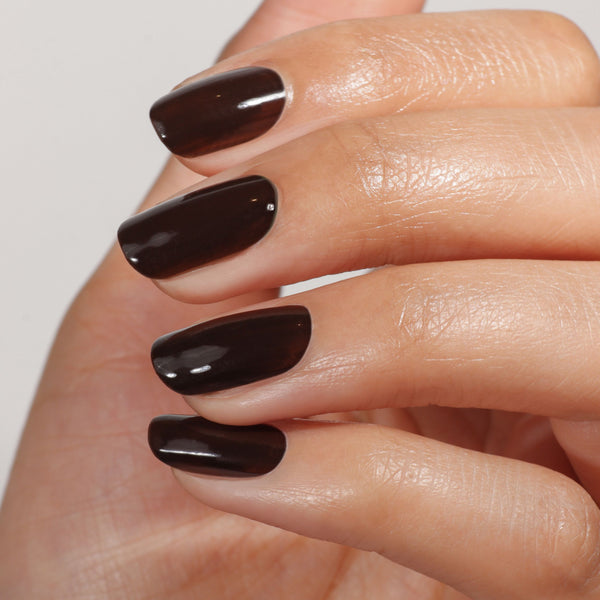 Hand with dark brown nail polish on a plain background