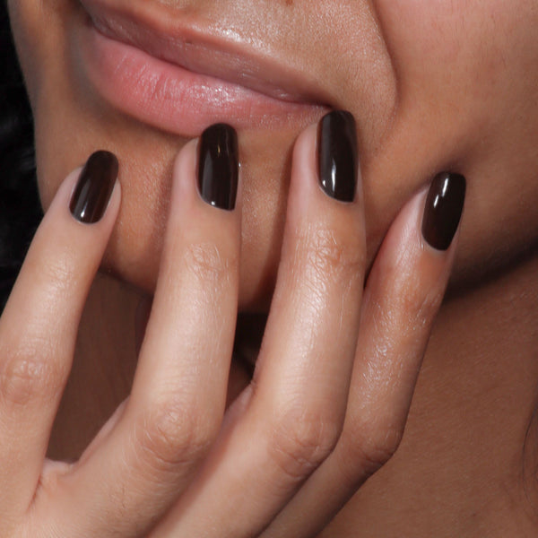 Close-up of a hand with dark nail polish against a neutral background