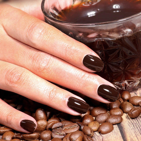 Hand with dark nail polish on coffee beans and a glass of coffee.