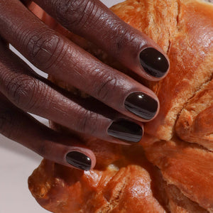 Hand with dark nail polish holding a piece of croissant
