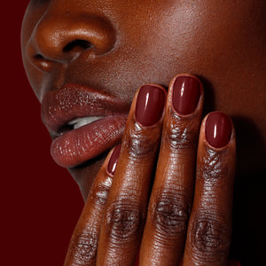 Close-up of a person's face and hand with dark red nail polish on a dark background