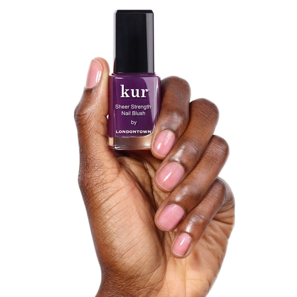 Purple nail polish bottle held by a hand with pinkish natural nails on a white background