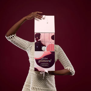 Person holding a 'All that glitters!' advent calendar against a dark red background