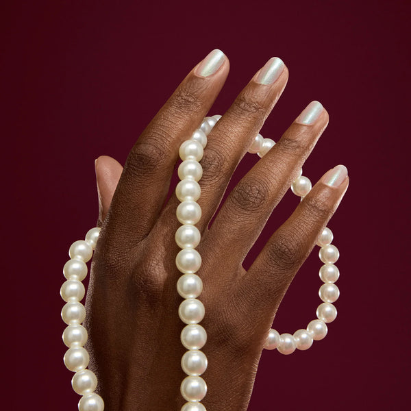 Hand holding a pearl necklace against a red background