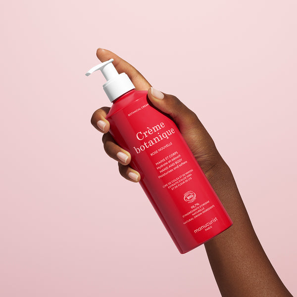 Hand holding a red bottle of Crème botanique with a pink background
