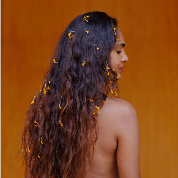 Woman with long, wavy hair adorned with small flowers against an orange background