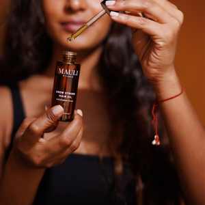 Woman holding a bottle of Mauli Rituals hair oil with a dropper.