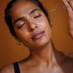 Woman applying a dropper of oil applied to her face against an orange background