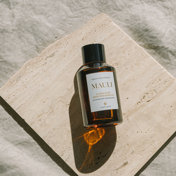 Glass bottle of MAULI RITUALS Surrender Vata Body Oil on a stone surface